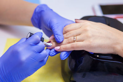 Close-up manicure master with sterile blue gloves paints nails with protective varnish to a woman 