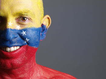 Close-up portrait of smiling man with venezuelan flag body paint against gray background