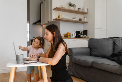 Toddler looking at shocked mother with laptop at home