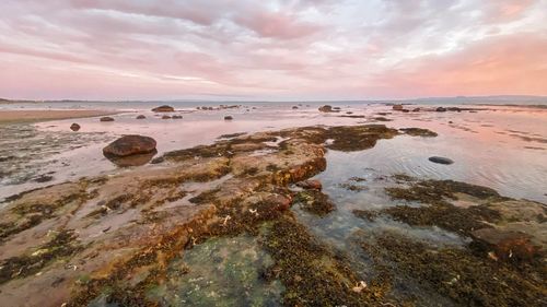 Rocks on beach against sky during sunset