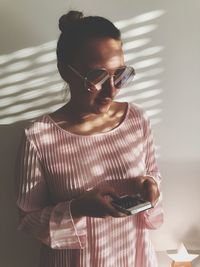 Young woman using mobile phone against wall