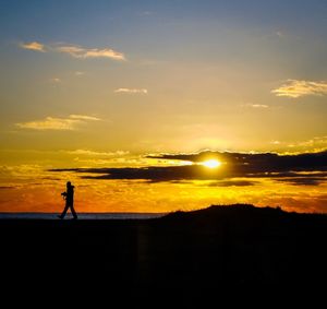 Silhouette man standing on orange sunset sky