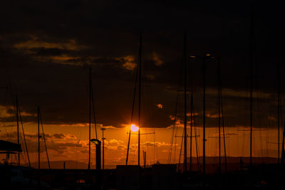 Silhouette sailboats on harbor against orange sky