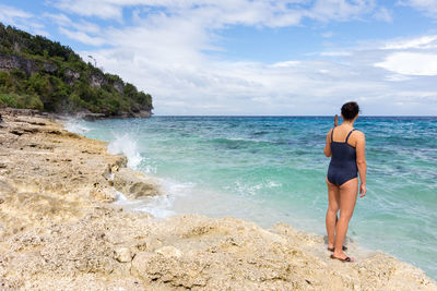 Rear view of woman standing on shore at beach against sky