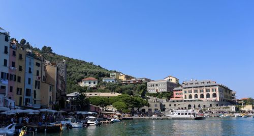 Sailboats in canal amidst buildings in town against clear blue sky