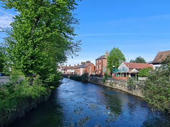 Arch bridge over river by buildings against blue sky