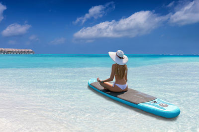 Rear view of woman meditating on surfboard in sea