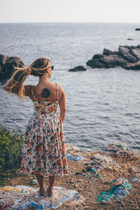 Rear view of woman holding her hair while standing on shore