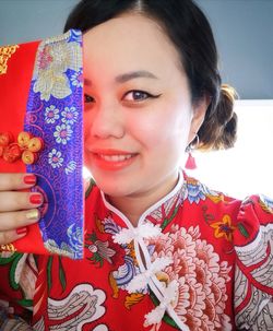 Close-up portrait of smiling young woman holding camera