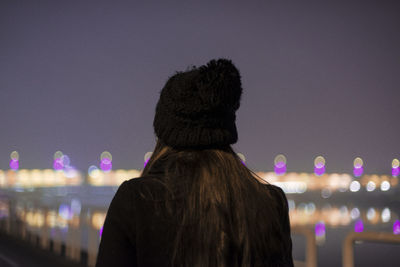 Rear view of woman against illuminated sea at night