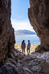 Rear view of people on rock by sea against sky