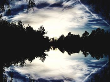 Silhouette trees by lake in forest against sky