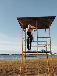 Woman standing in lifeguard hut at beach against sky