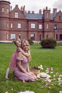 Beautiful young mother with daughter in pink dresses sitting on a green meadow in summer. pet rabbit