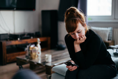 Young woman using mobile phone while sitting on table