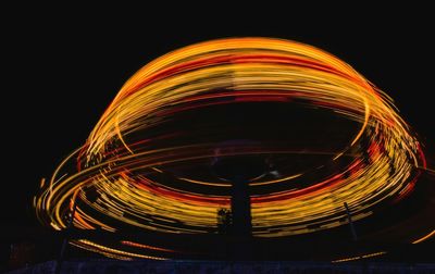 Light trails at amusement park against sky at night