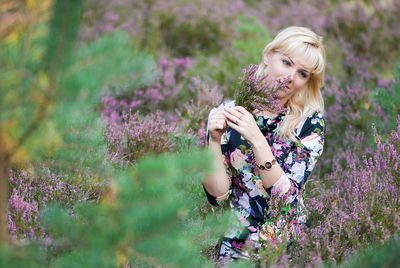 Thoughtful woman holding bunch of flowers while kneeling on field