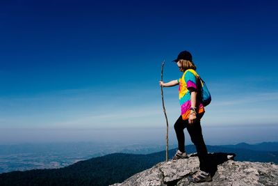 Full length of woman holding stick while standing on mountain against sky