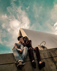 Low angle view of friends sitting on built structure against sky