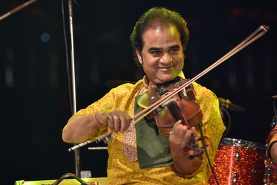 Smiling man playing violin while sitting on stage