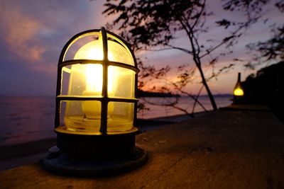 Close-up of illuminated lamp in sea against sky during sunset