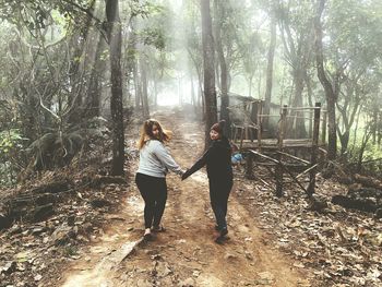 Rear view of women standing amidst trees in forest