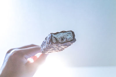 Cropped hand on person holding ice cream bar against clear sky in sunny day