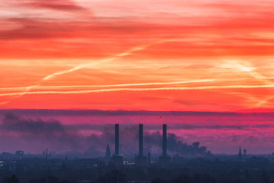 Smoke emitting from factories against dramatic sky during sunset