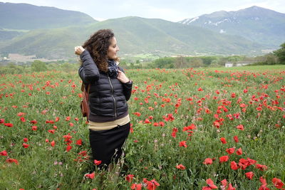 Smiling young woman standing on field with flowering plants against sky