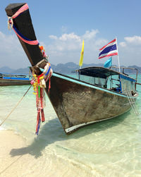 Longtail boat moored on shore against sky