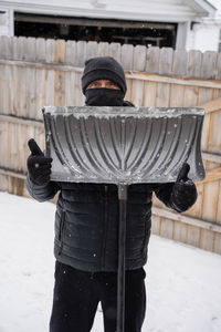 Man holds a snow shovel and gives you a thumbs up while he clears your driveway