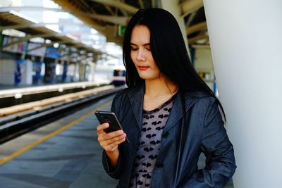 Woman using phone while standing at railroad station