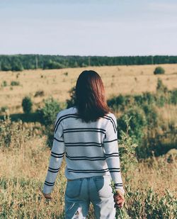 Rear view of young woman standing on grassy field against sky