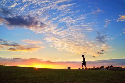 Silhouette woman standing on field against sky during sunset