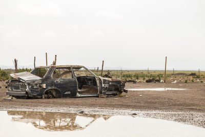 Old abandoned car on field against sky