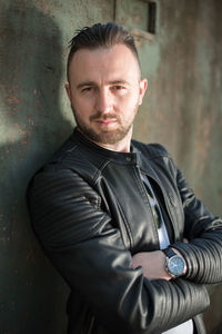 Portrait of young man in leather jacket standing by abandoned train