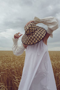 Woman wearing hat standing on field against sky