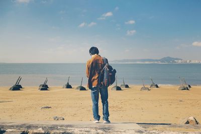 Rear view of men standing on beach against sky