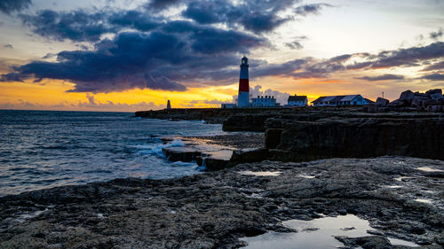 Lighthouse by sea against sky during sunset
