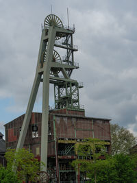 Low angle view of crane by building against sky