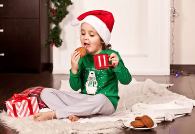 Portrait of cute girl holding gift while sitting on bed at home