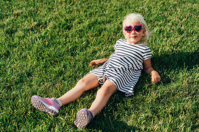 Little stylish girl in sunglasses lies on the lawn