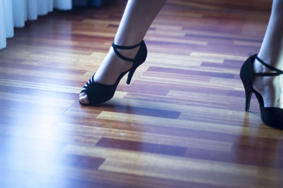 Low section of woman wearing high heels standing on hardwood floor