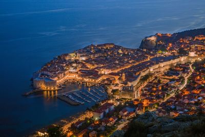 High angle view of illuminated cityscape by sea against sky