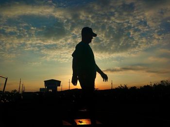 Silhouette man walking against cloudy sky during sunset