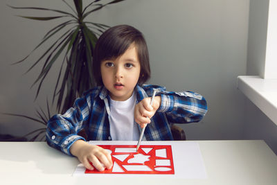 Boy child draws on paper with a ruler on a table sitting by the window