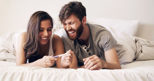 Happy couple looking at pregnancy kit lying on bed