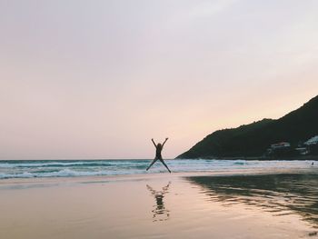 Man surfing in sea against sky during sunset