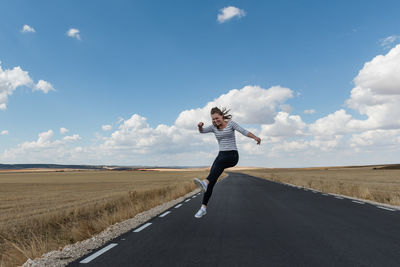 Woman jumping on road against sky