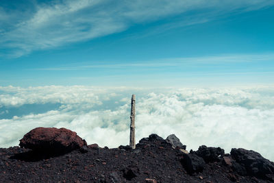 Wooden pole on rocky mountain against cloudscape